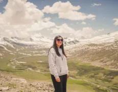 A smiling female tourist standing in front of snow-covered mountain peaks at Babusar Top in Naran Kaghan