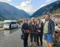 Two foreign couples standing on a mountain road near a Grand Cabin van with lush green mountains in Naran Kaghan
