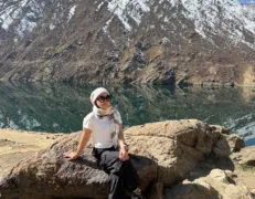 Foreign female traveler sitting on a rock with a scenic snow-capped mountain and alpine lake in Naran Kaghan