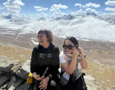Two foreign female tourists sitting on a rock laughing with a distant river and snow-capped mountains near Babusar Top