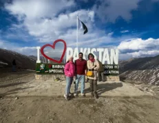 Two foreign female tourists and a male traveler posing in front of the I Love Pakistan sign at Babusar Top