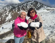 Two foreign female tourists holding snowballs and smiling at Babusar Top in Naran Kaghan Valley