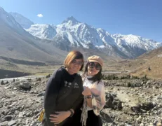 Two foreign female tourists posing against a backdrop of snow-covered peaks and brown hills in Naran Kaghan Valley