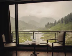 Hotel room balcony view showing two chairs overlooking a river and cloud-covered mountains in Naran Valley