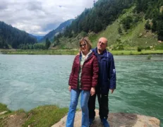 International couple standing on a rock beside a scenic river and lush green mountains in Naran Kaghan