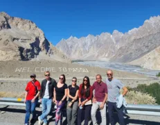 Couple pausing for a photo near the roadside Passu welcoming marker