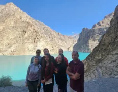 Group of couples and their mountain guide posing together by the turquoise reservoir shore