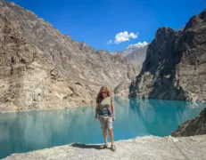 Sightseer balancing on a shoreline boulder surrounded by bright blue glacier-fed water