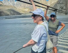 Two friends carefully crossing the wooden planks of Hussaini Suspension Bridge over the river