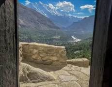 Scenic Mountain View from Baltit Fort Window Scenic view of snow-covered mountains and green forest seen through a window at Baltit Fort in Karimabad Hunza